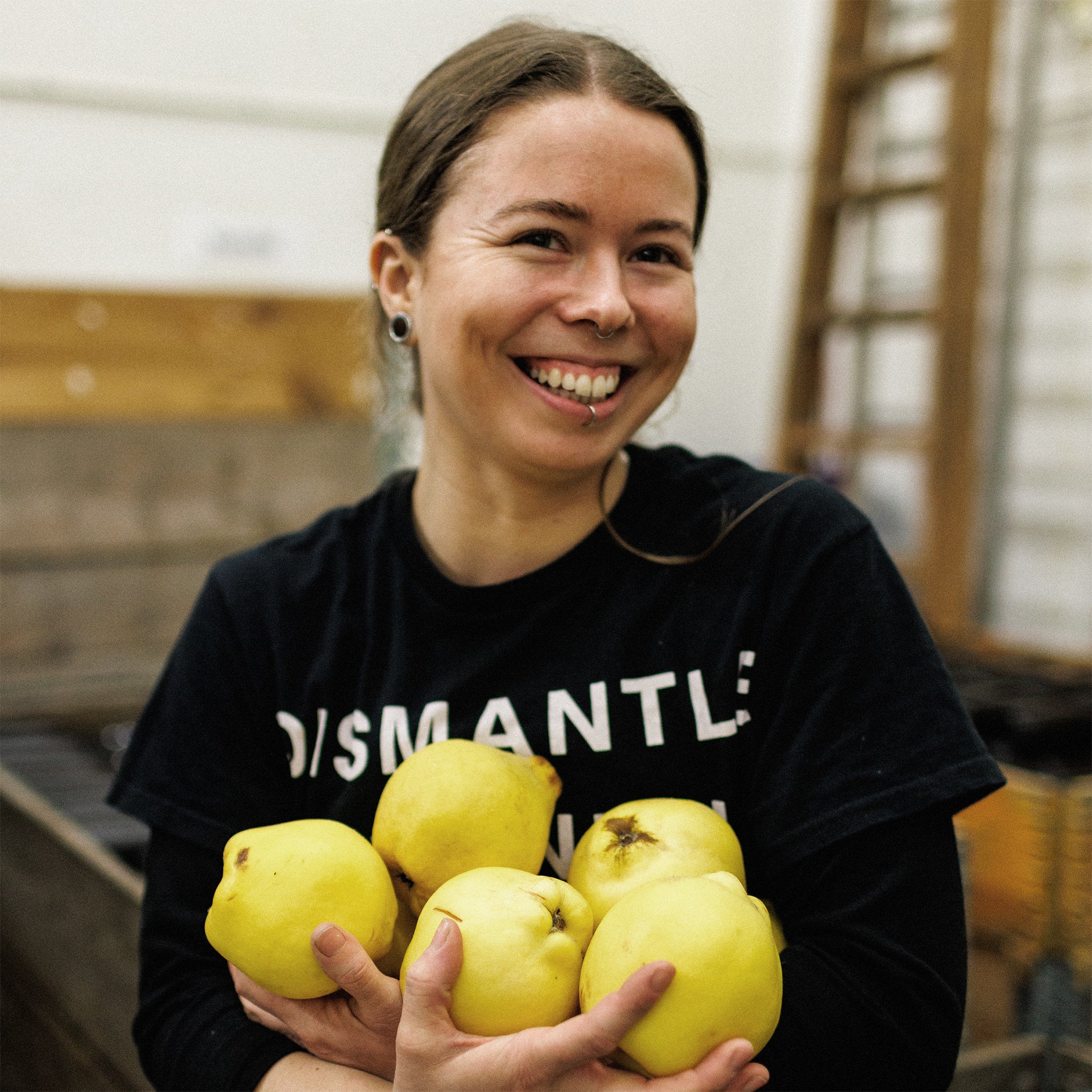 Person holding quince, wearing a black t-shirt with white text, indoors.