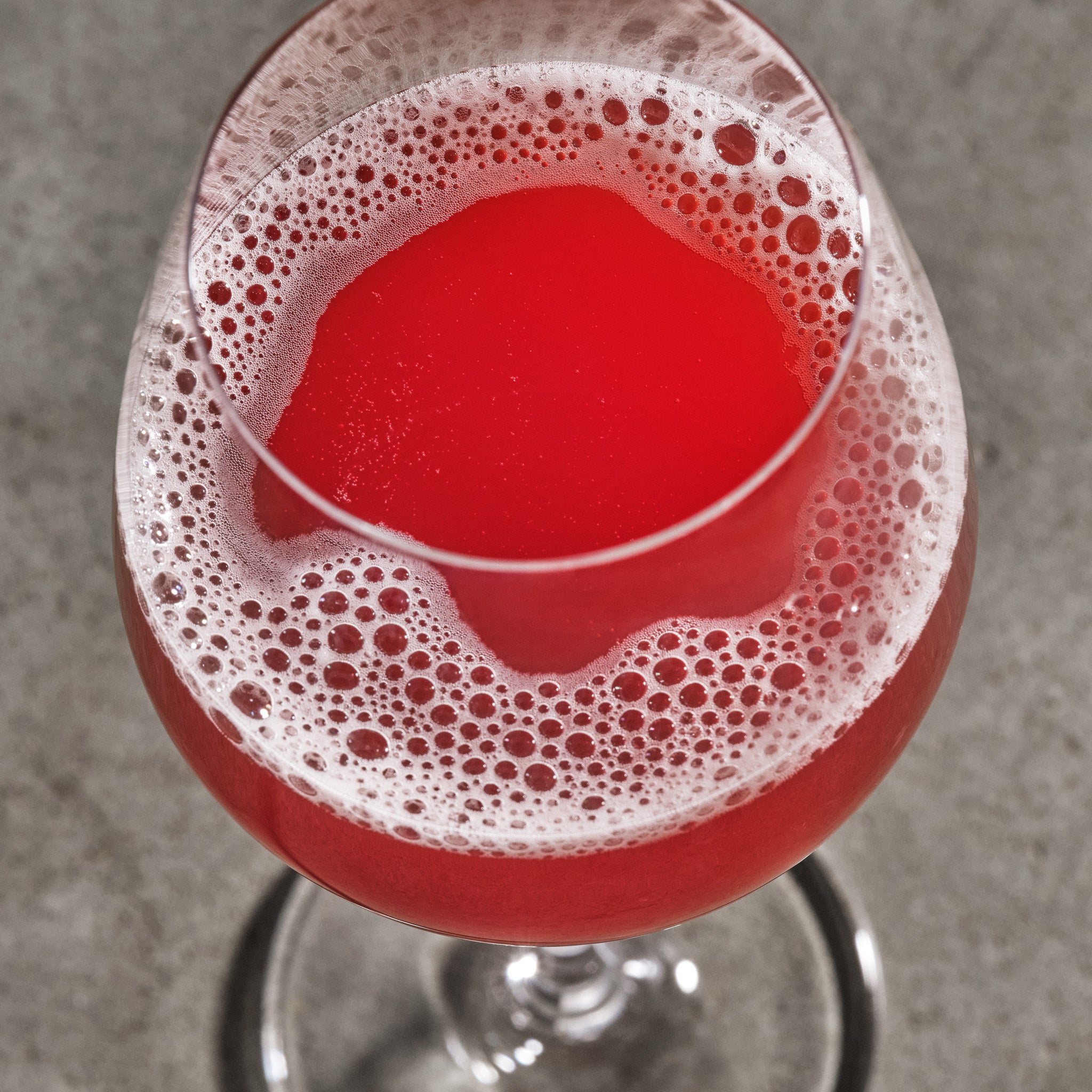 Red non-alcoholic wine with foam in a glass on a gray background