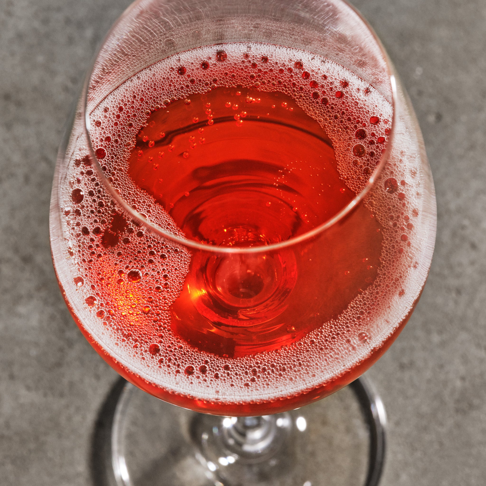 Close-up of a glass filled with red liquid and foam on a gray background