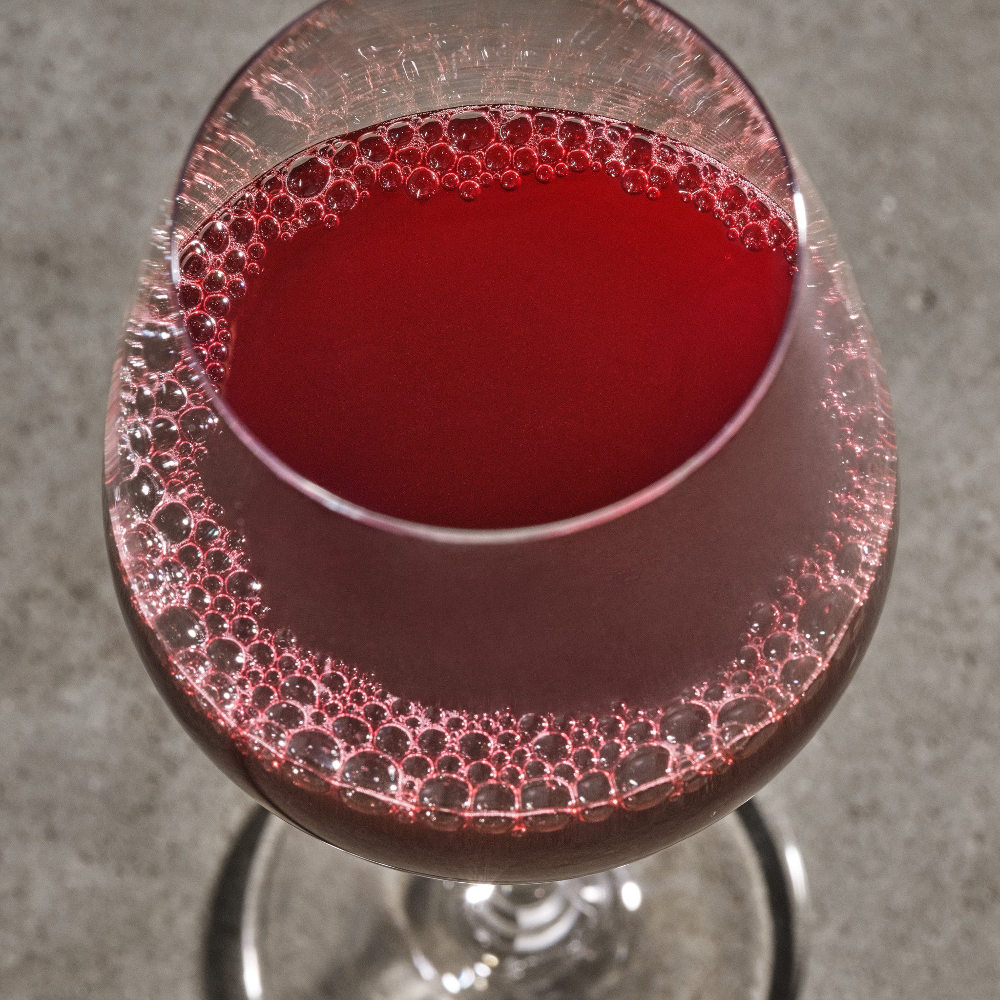 Close-up of a glass with red liquid and bubbles on a gray surface