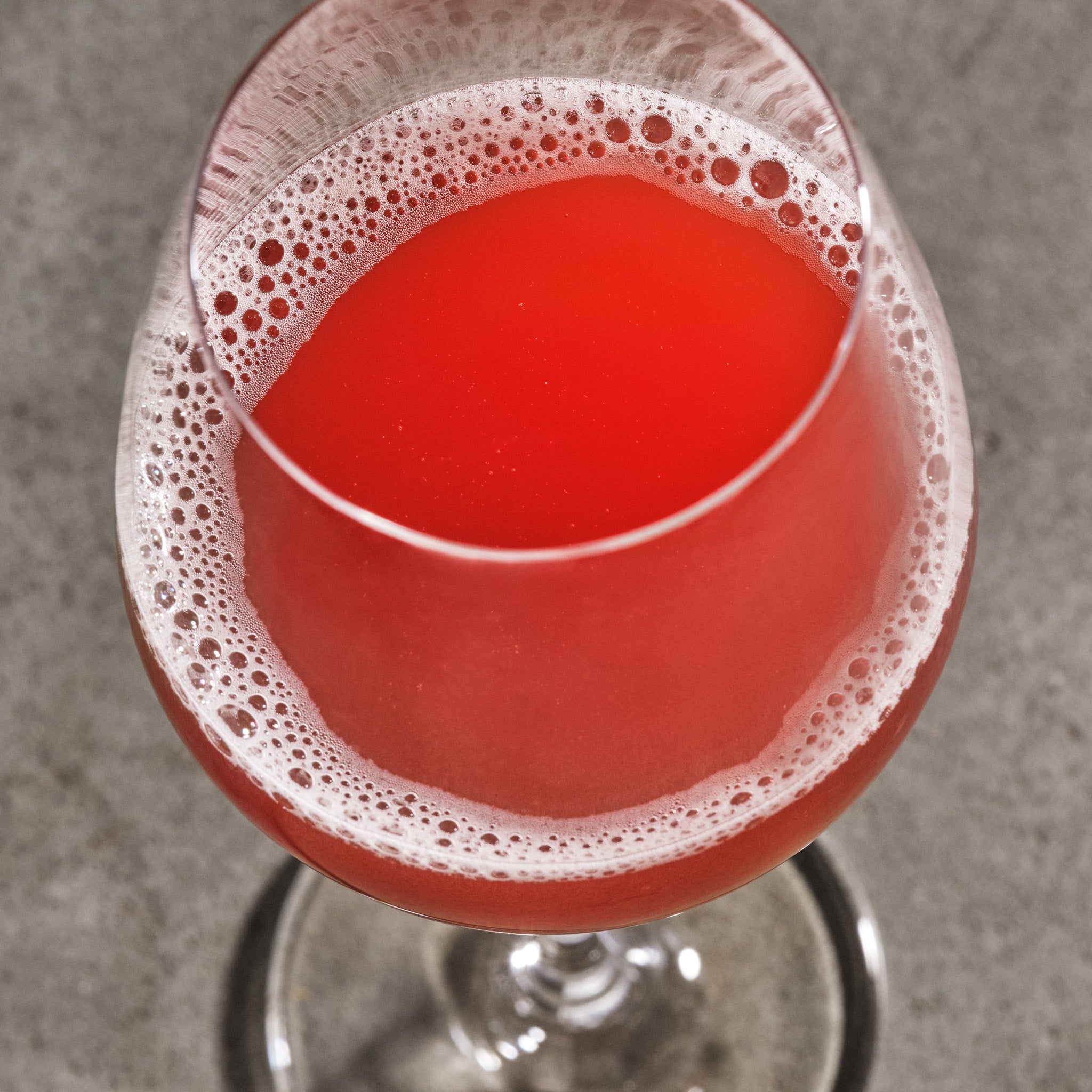 Red non-alcoholic wine with foam in a glass on a gray background